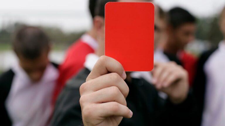 Referee showing a red card to players during an outdoor soccer game.